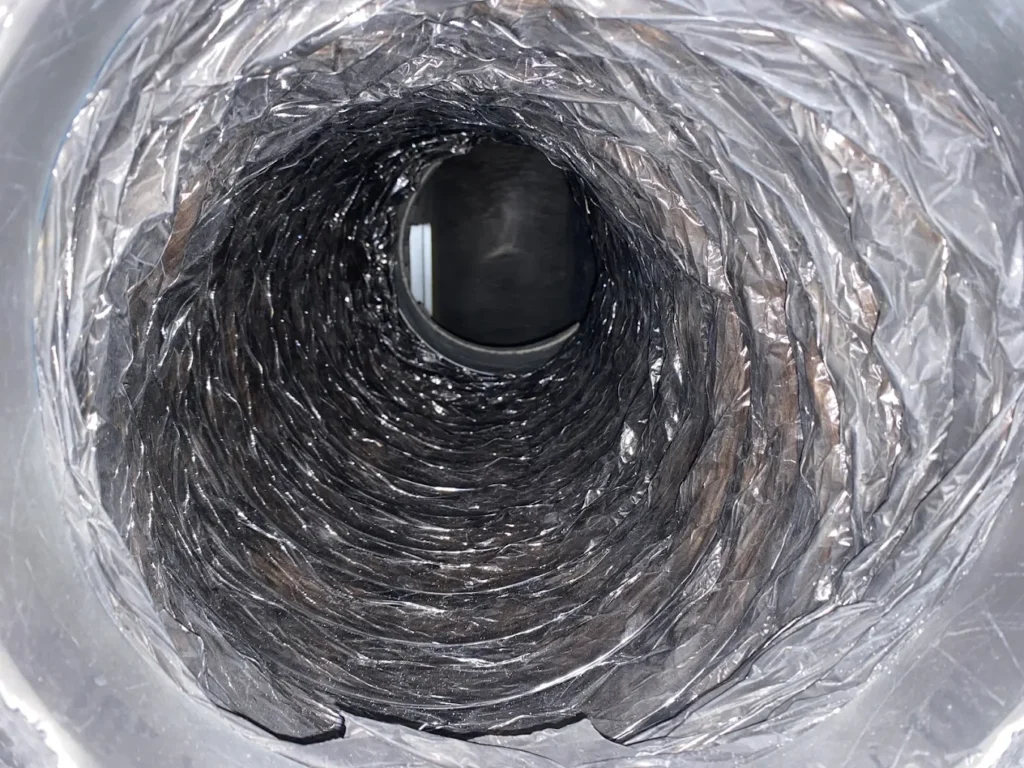 Reflective foil duct interior with crinkled metallic insulation, concentric folds, and dark circular opening.