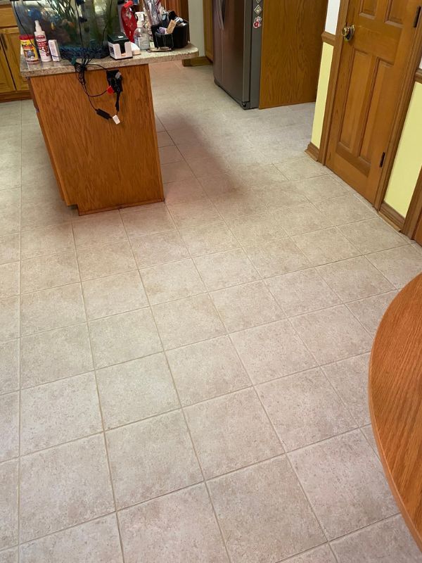 Clean beige tiled kitchen floor with wooden island, open doors, and warm adjoining hallway.