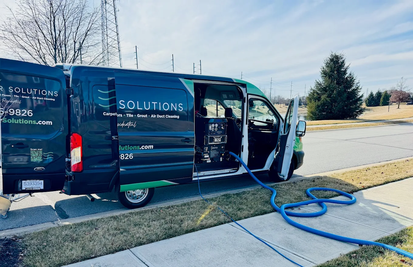 Healthy Interior Solutions cleaning service van with open doors and blue hose at a job site.
