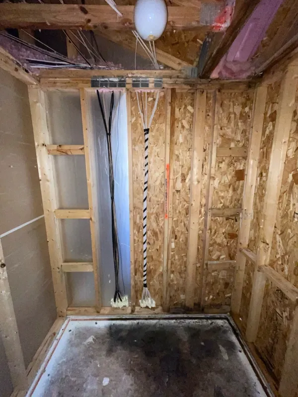 Unfinished closet renovation with exposed studs, wiring, ceiling beams, pink insulation, and dusty concrete floor.