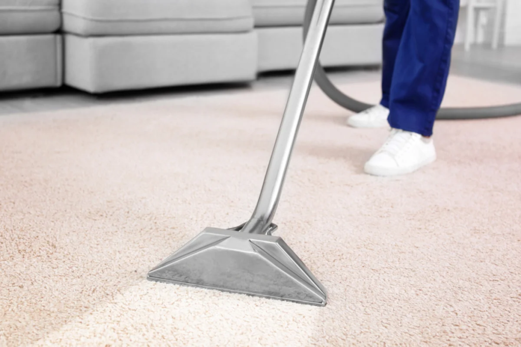 Professional cleaner using an extraction machine on beige carpet in a bright modern living room.