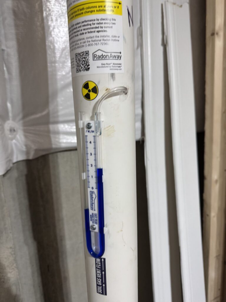 White radon testing device with technical labels, QR code, radiation symbol, and blue markings.