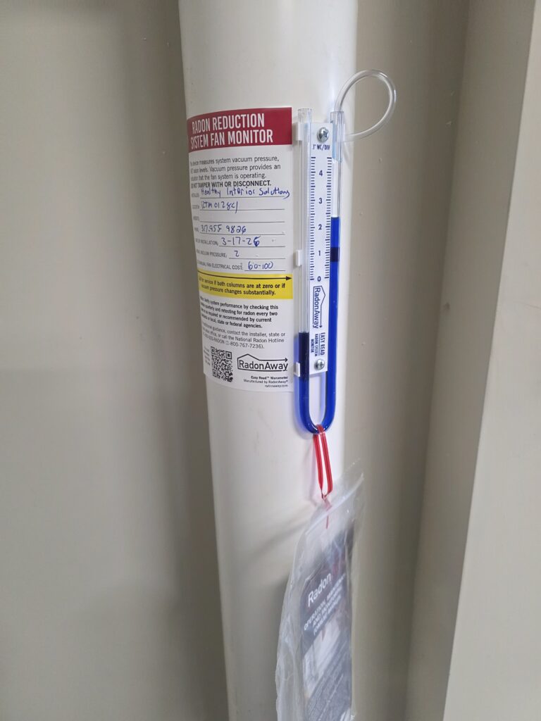 Radon U-tube manometer in a wall recess with tubing, wires, and protective sleeve.