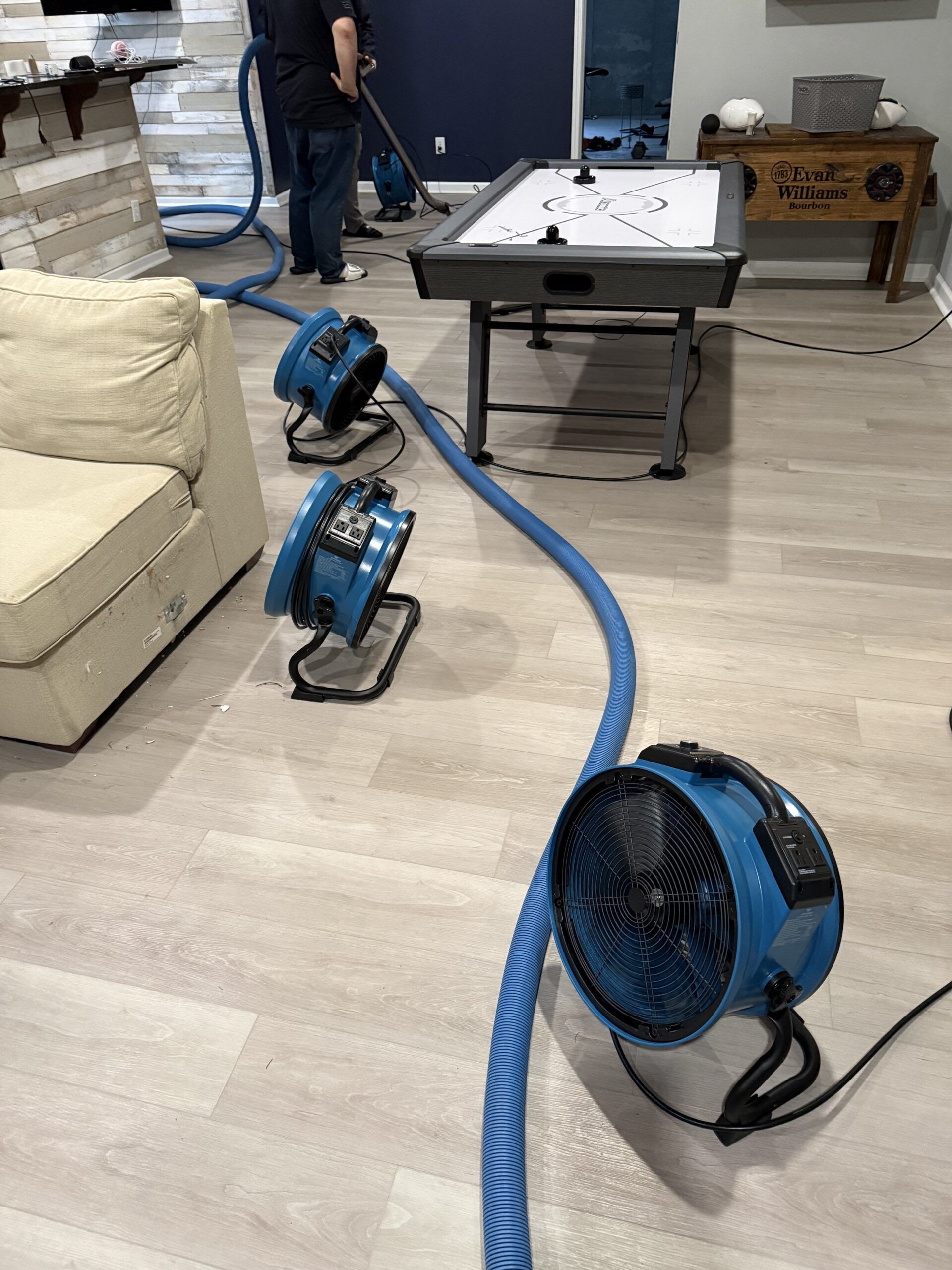 Water damage restoration fans and hoses dry a residential room with a game table.
